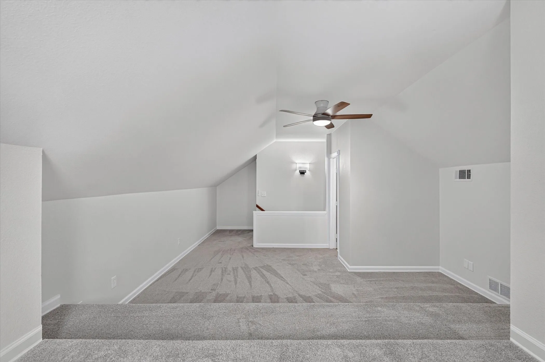 2nd floor Expansive carpeted loft space featuring sloped ceilings, a ceiling fan with light, and wall-mounted lighting fixtures