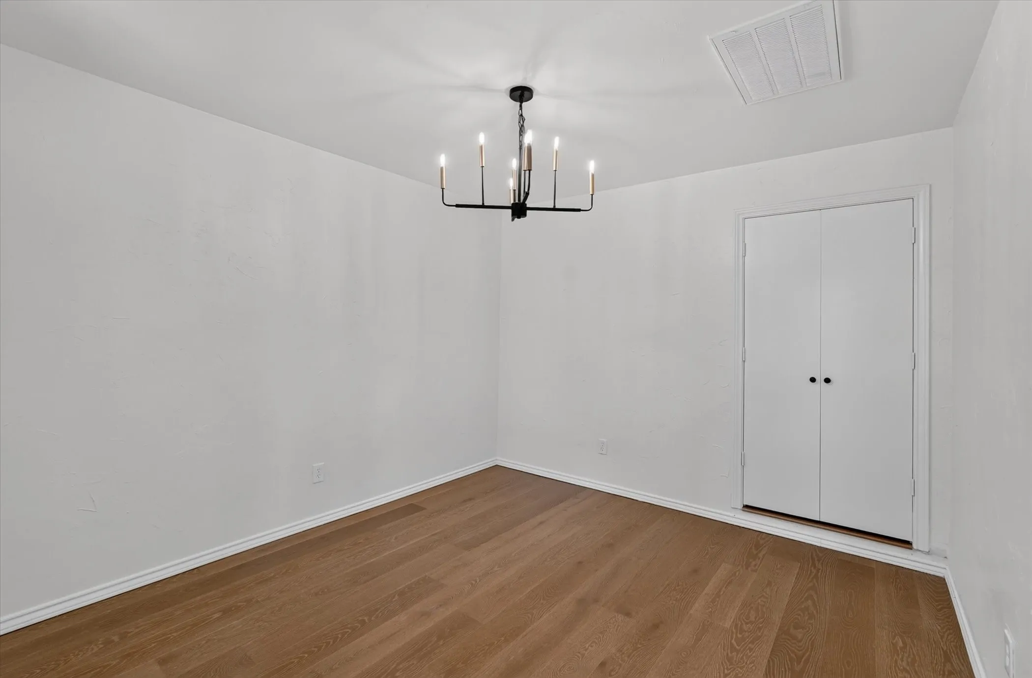 Wood-finish flooring with white baseboards, white walls, and a black chandelier