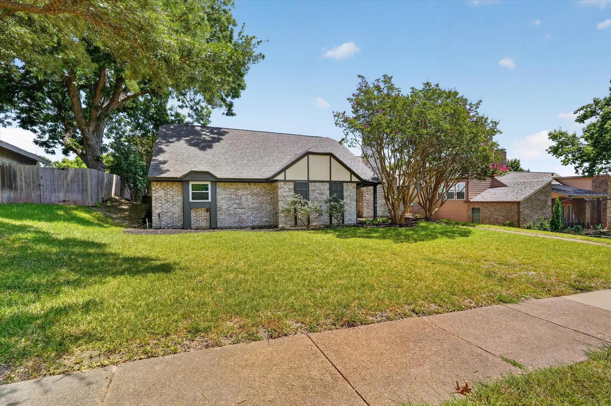 Brick and stucco exterior with dark trim accents, featuring a pitched roofline and mature front yard landscaping