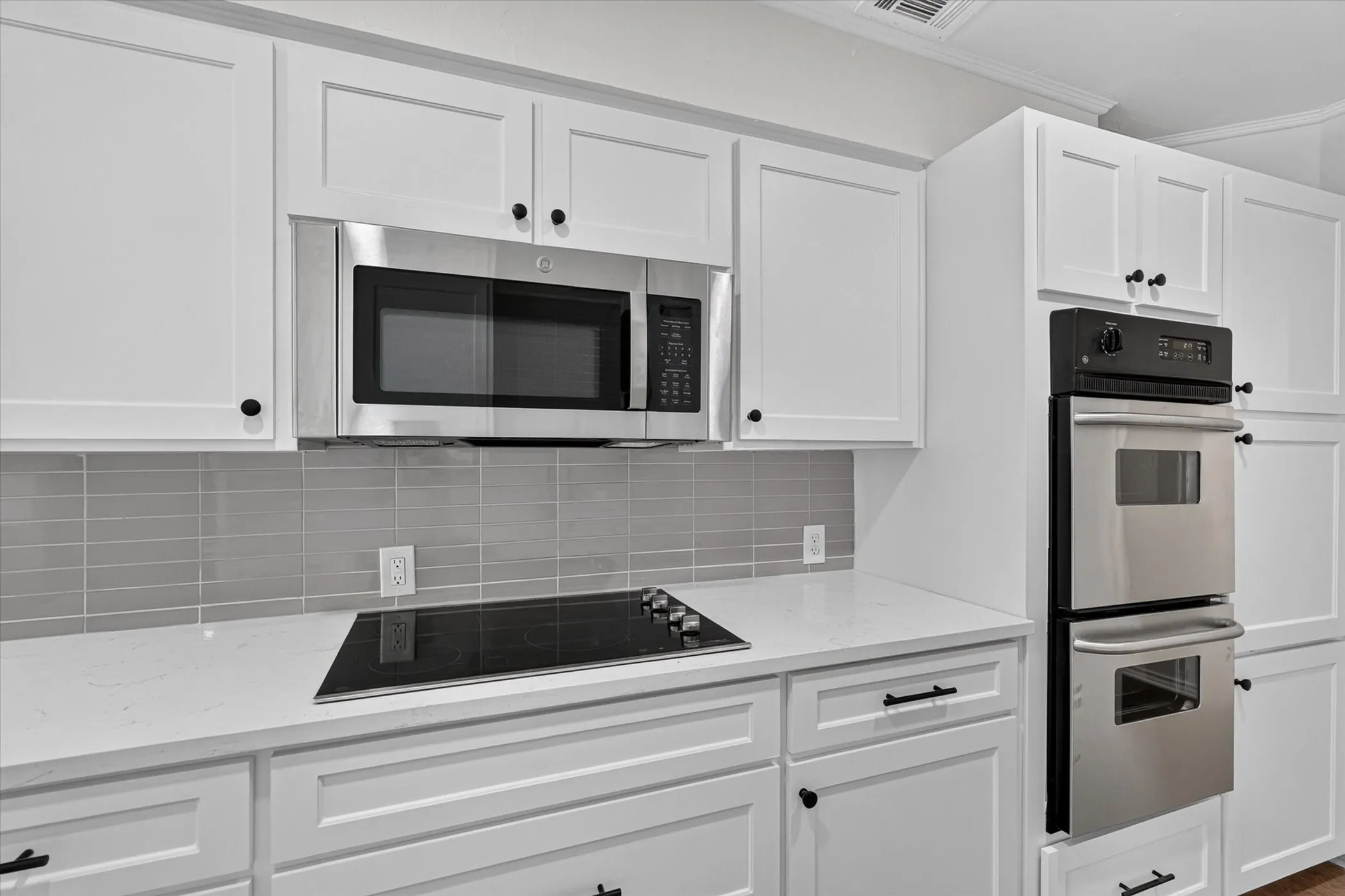 White shaker cabinetry, stainless steel microwave, integrated cooktop, stainless steel double wall oven, and light-toned backsplash