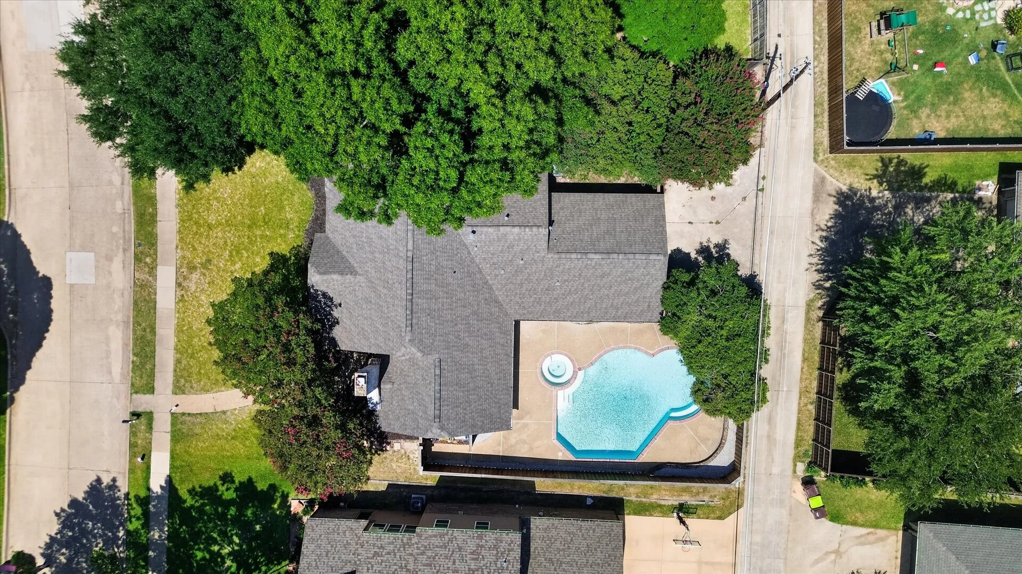 Shingle roof, mature landscaping, and an irregularly shaped in-ground pool with a spa