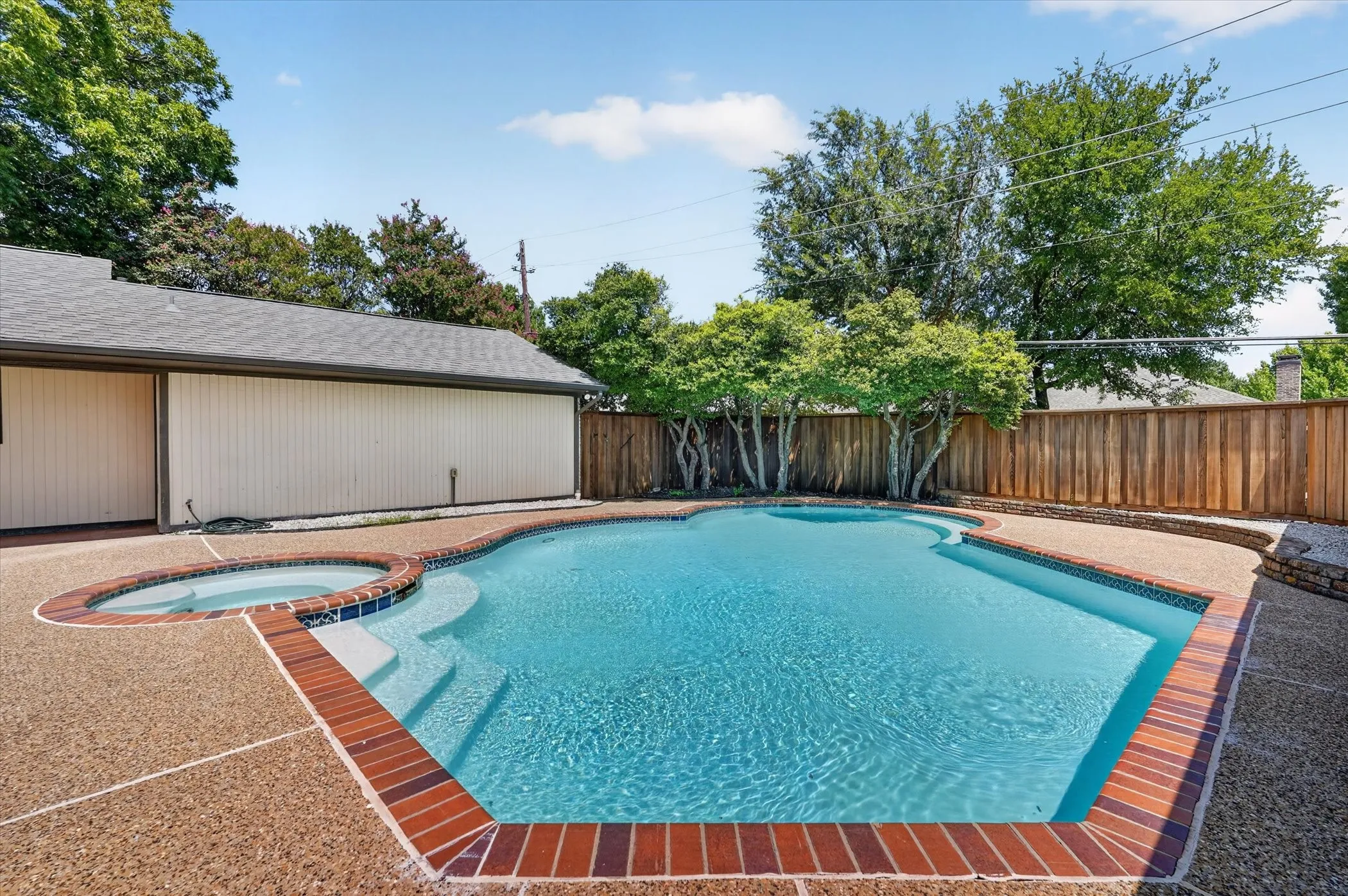 Freeform swimming pool featuring integrated spa, brick coping, and exposed aggregate decking