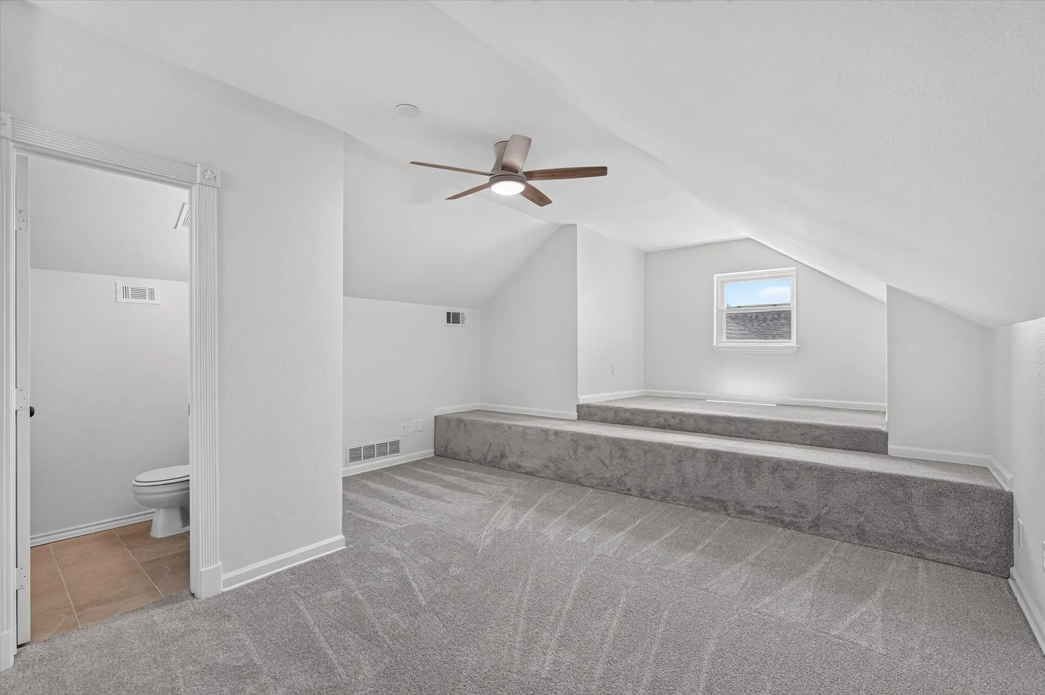 2nd floor Sloped ceilings with a ceiling fan, gray carpet flooring, elevated carpeted platforms, and a window with a white frame