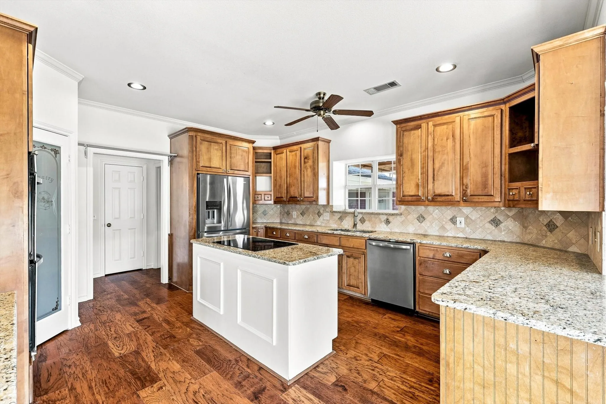 Kitchen featuring wood-finish flooring, a center island with a cooktop, granite countertops, wood cabinetry, and stainless steel appliances