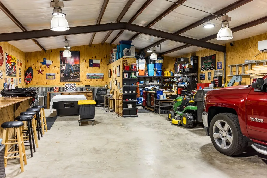 Spacious interior with exposed structural beams, plywood wall finishes, concrete flooring, and multiple ceiling-mounted light fixtures