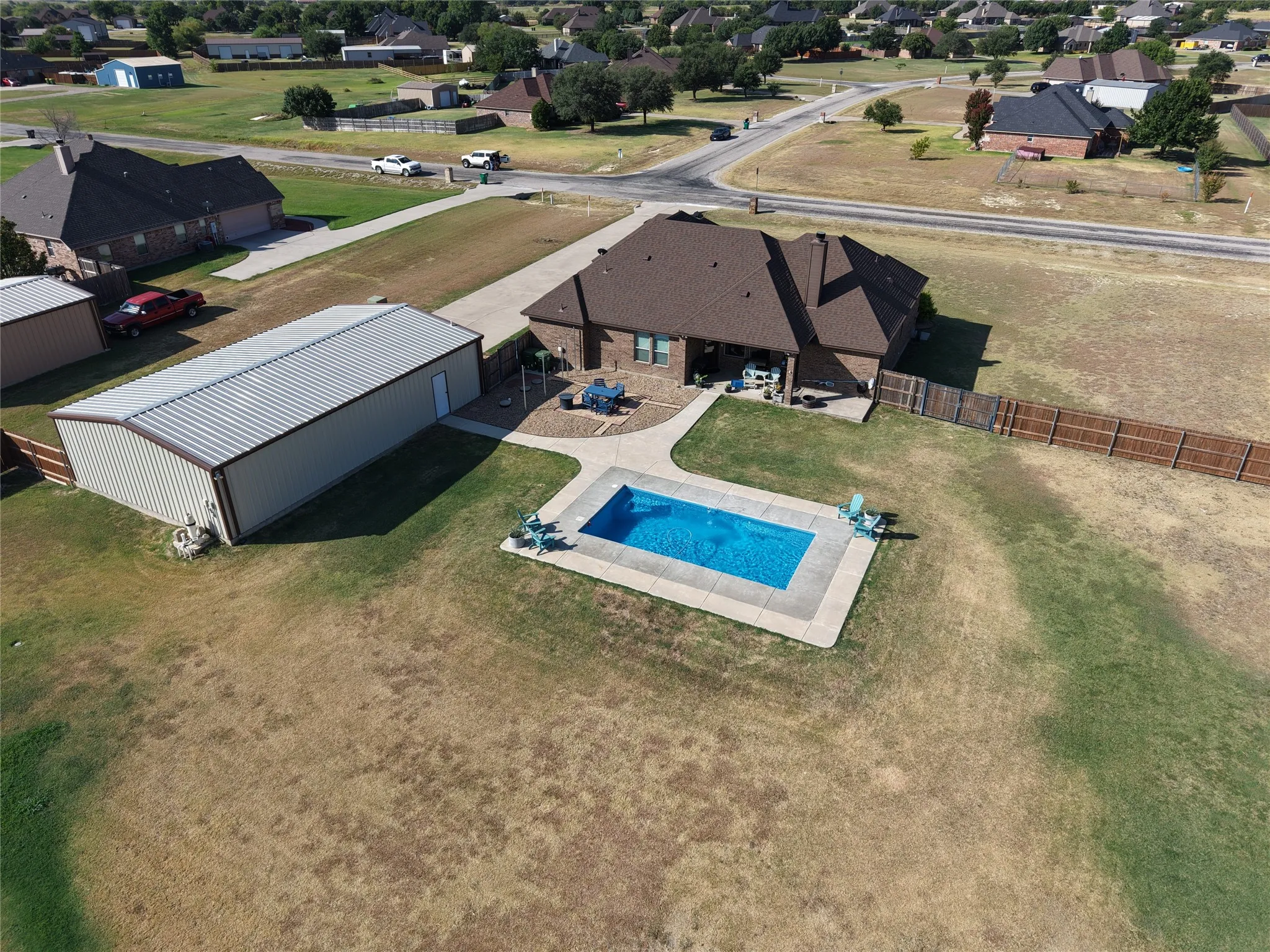Expansive rural property featuring a substantial brick residence with covered patio entertaining space, a metal-frame agricultural outbuilding, sparkling in-ground swimming pool with concrete decking, manicured lawn, and mature landscaping.