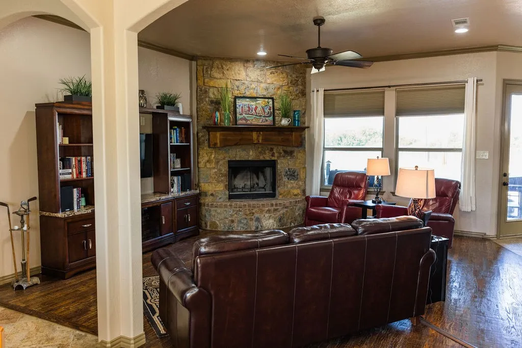 Stone-clad corner fireplace with a wood mantle, wood-finish flooring, ceiling fan, recessed lighting, and built-in cabinetry