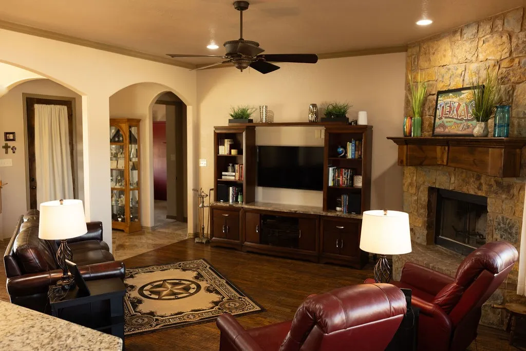 Stone-faced fireplace with a wood mantel, dark wood-finish flooring, recessed lighting, ceiling fan, and built-in entertainment center