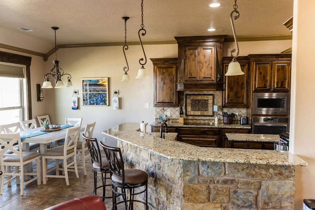 Kitchen featuring stone-clad breakfast bar, granite countertops, wood cabinetry, stainless steel appliances, and tile backsplash