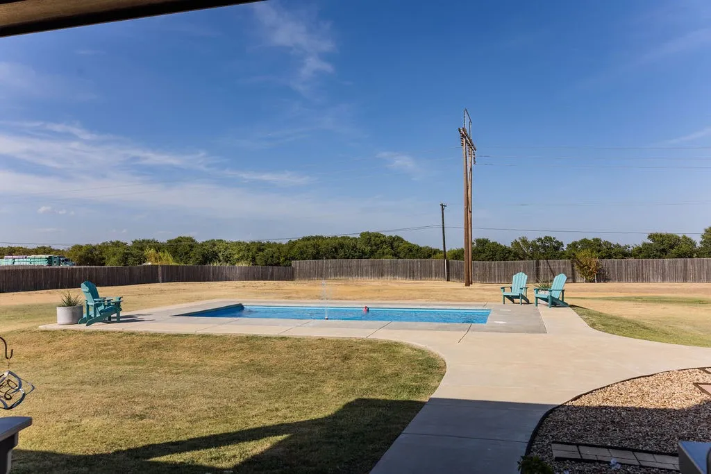 In-ground swimming pool with a concrete surround, privacy fencing, and a concrete pathway
