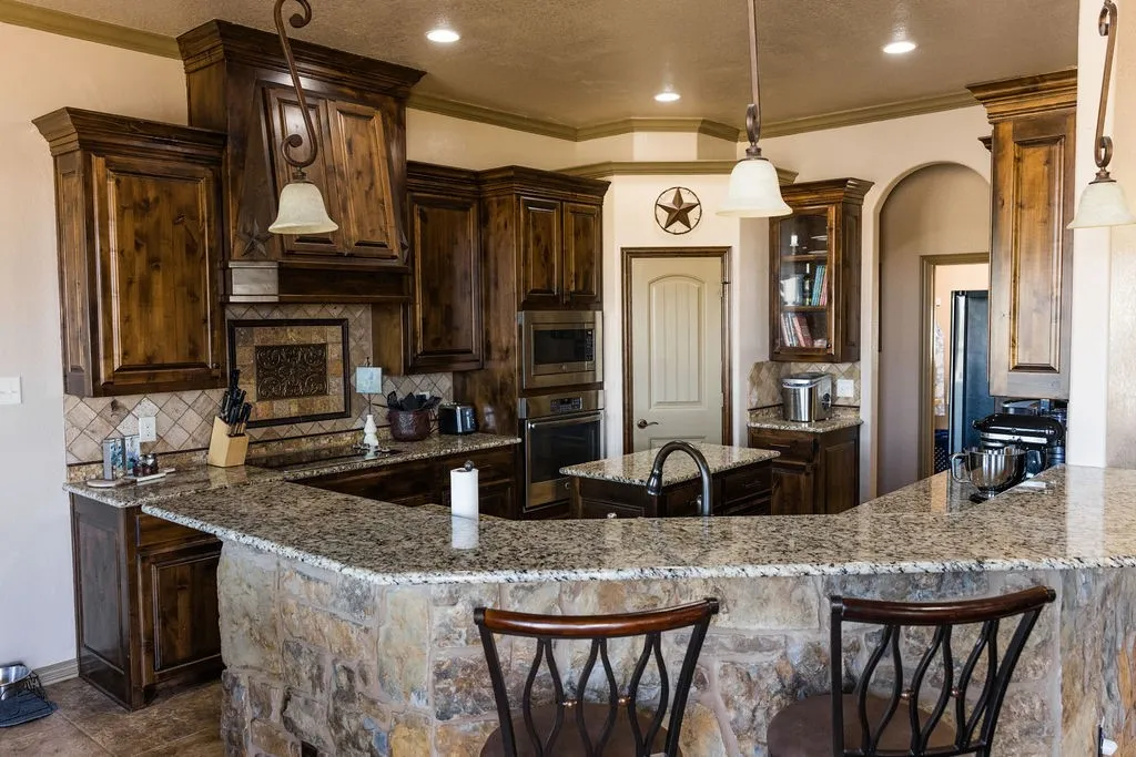 Kitchen featuring wood-finish cabinetry, stone countertop, stone-clad breakfast bar, built-in appliances, and pendant lighting