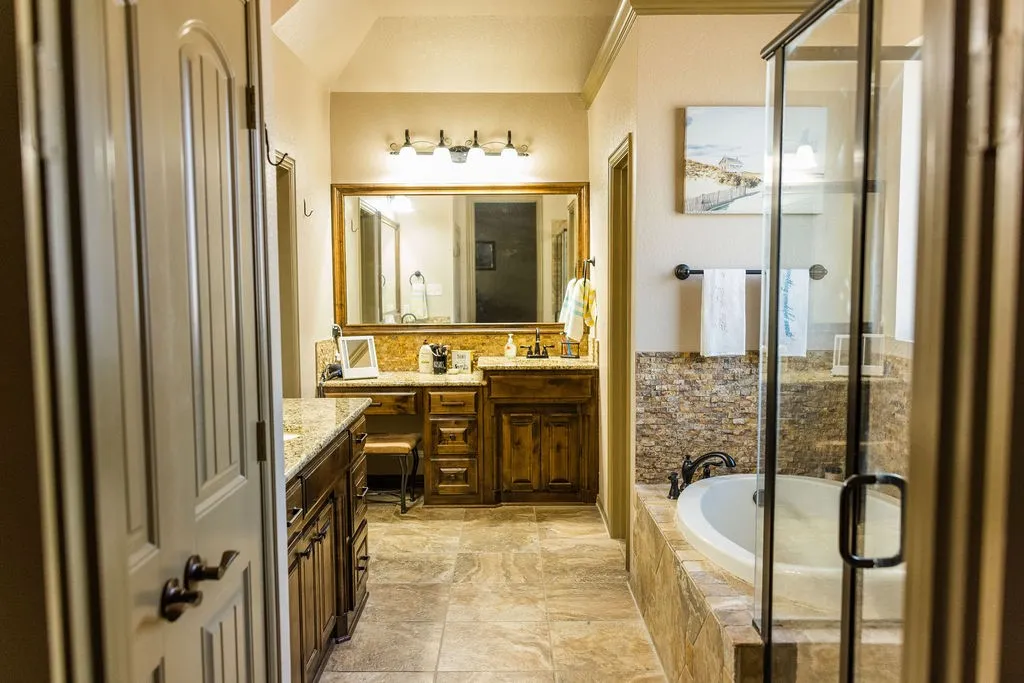 Bathroom featuring dual vanity with granite countertops, wood cabinetry, built-in soaking tub, and enclosed shower