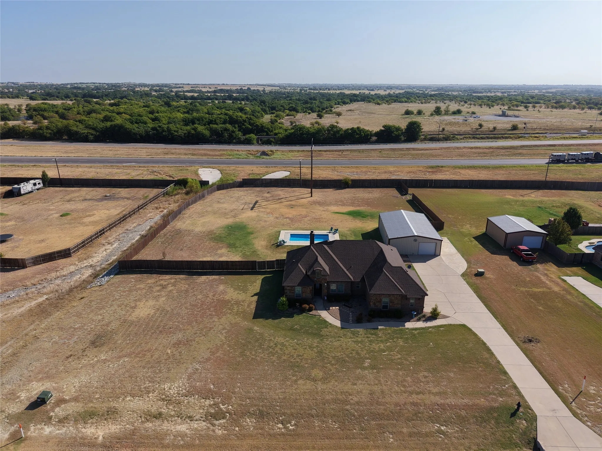 Stone and brick exterior residence featuring an extensive concrete driveway, a swimming pool, detached metal outbuildings.