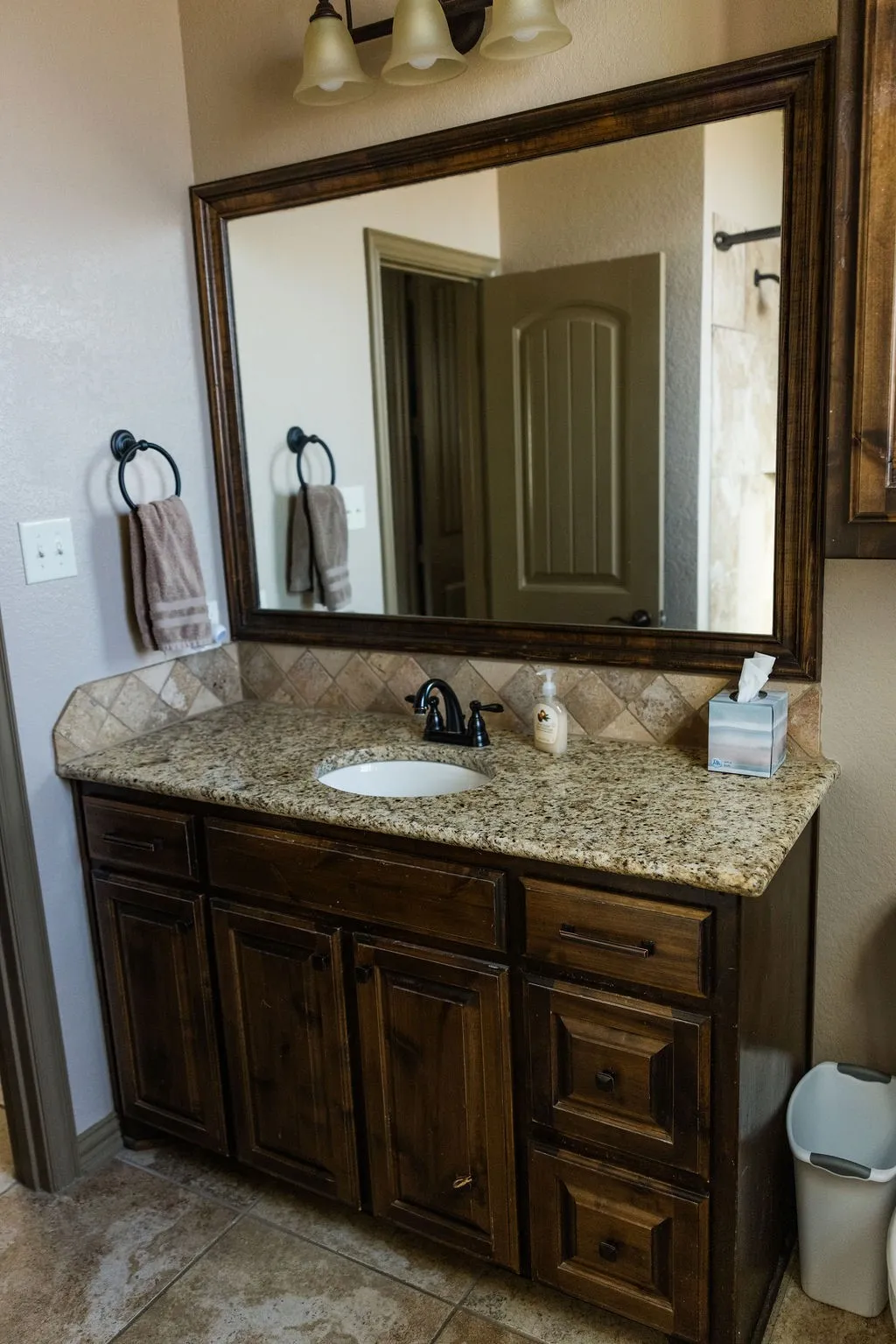 Vanity featuring a dark wood finish, a speckled countertop, an undermount sink, and a tiled backsplash