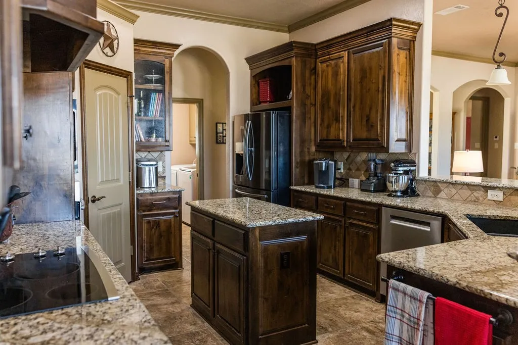 Kitchen featuring rich wood cabinetry, granite countertops, tile backsplash, and a central island