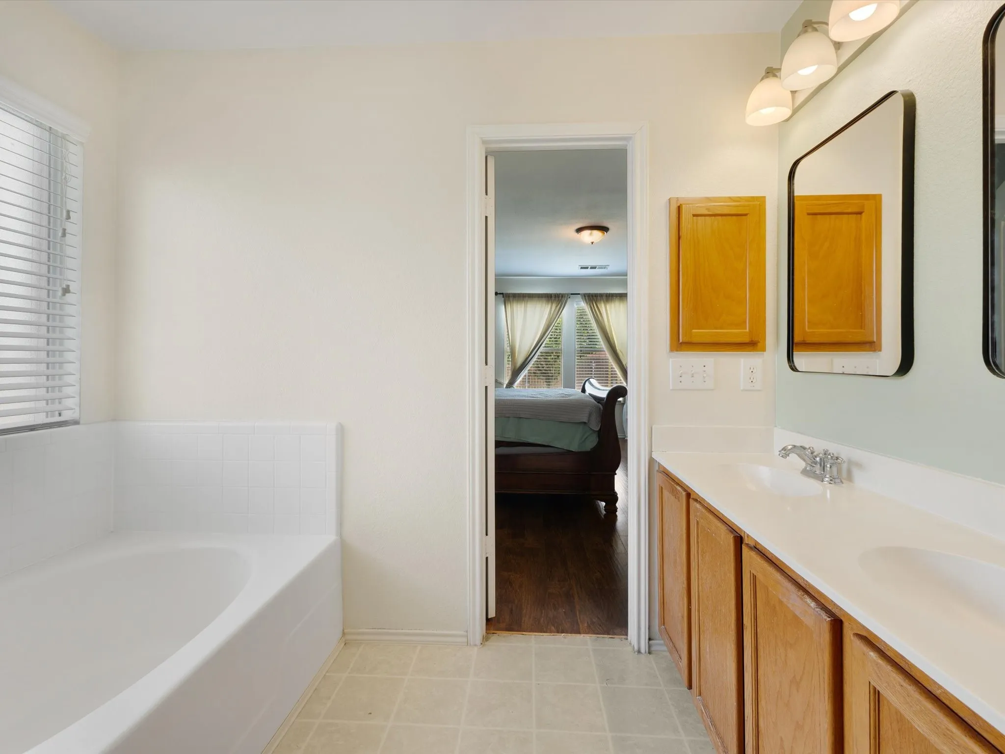 Spa-inspired primary bathroom featuring a soaking tub, dual vanity with wood cabinetry and white countertop, recessed lighting, and tile flooring