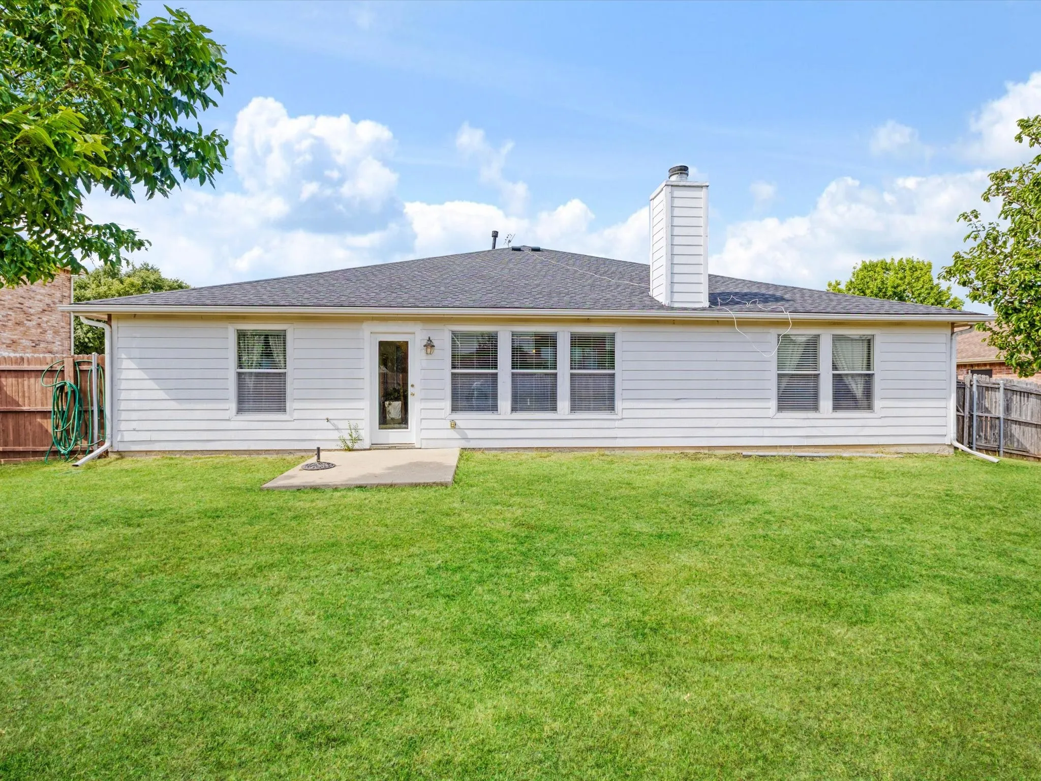 Expansive backyard with a manicured lawn, white siding exterior, dark shingle roof, and a concrete patio
