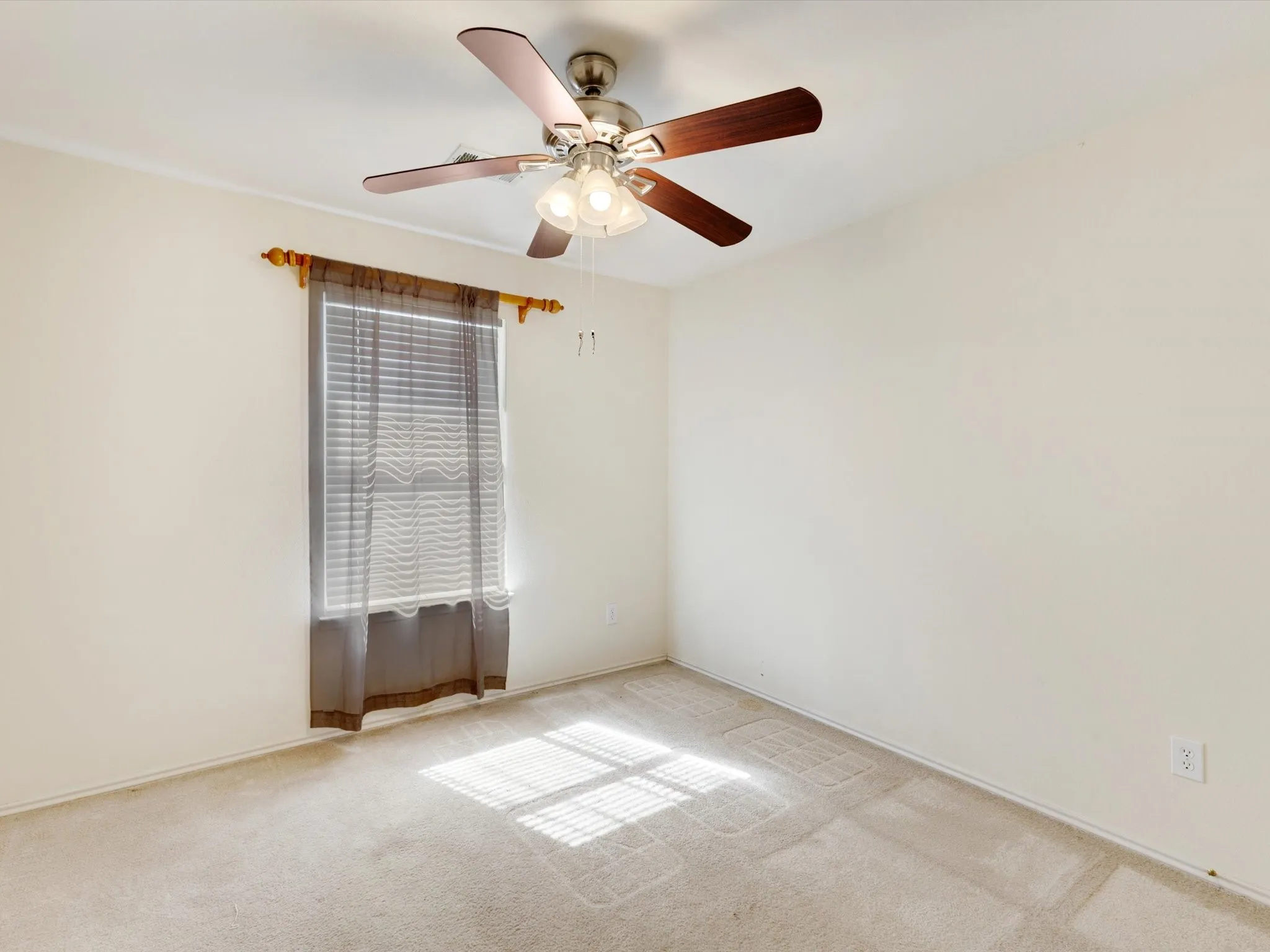 Light-colored carpeting with a window and a ceiling fan with integrated lighting