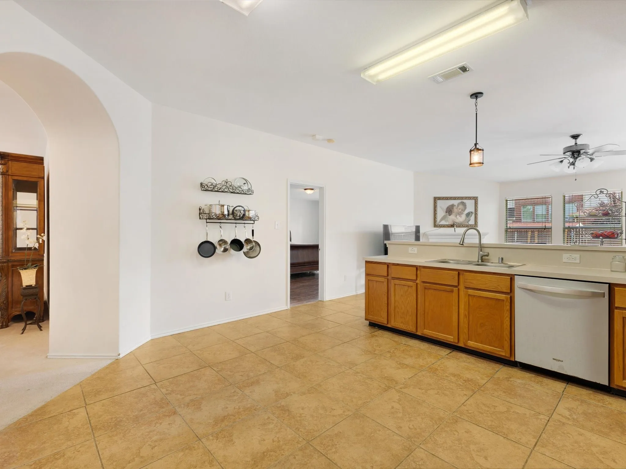 Kitchen featuring tile flooring, light wood-finish cabinetry, a stainless steel sink with a gooseneck faucet, and integrated dishwasher