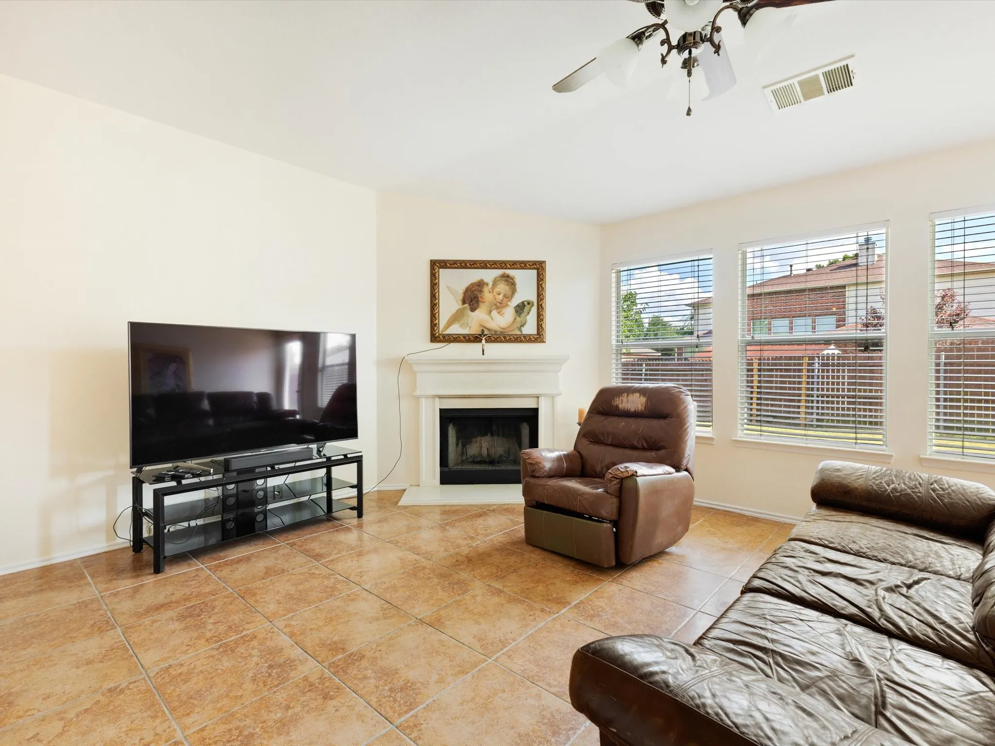 Corner fireplace with a mantle, multiple windows with blinds, ceiling fan, and tile flooring