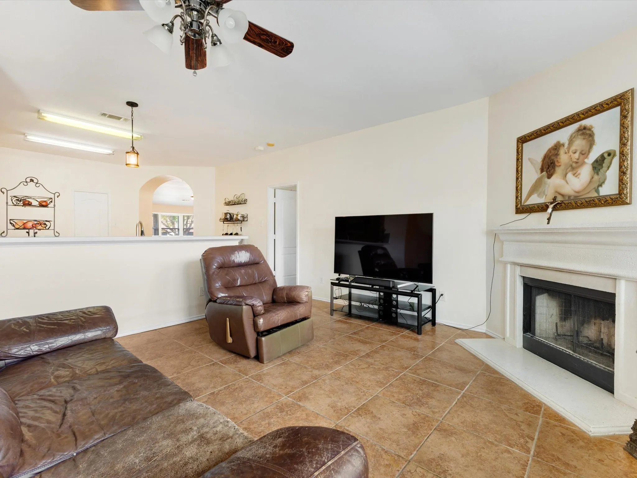 Tile flooring, fireplace with mantel, recessed arched entryway, ceiling fan with light fixture, and pendant lighting