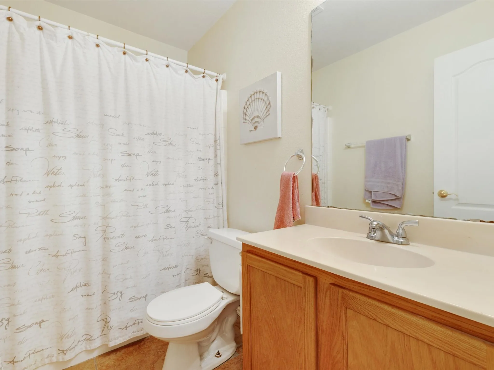 Bathroom featuring a wood-finish vanity with an integrated sink, a chrome two-handle faucet, a wall-mounted mirror, and a white toilet