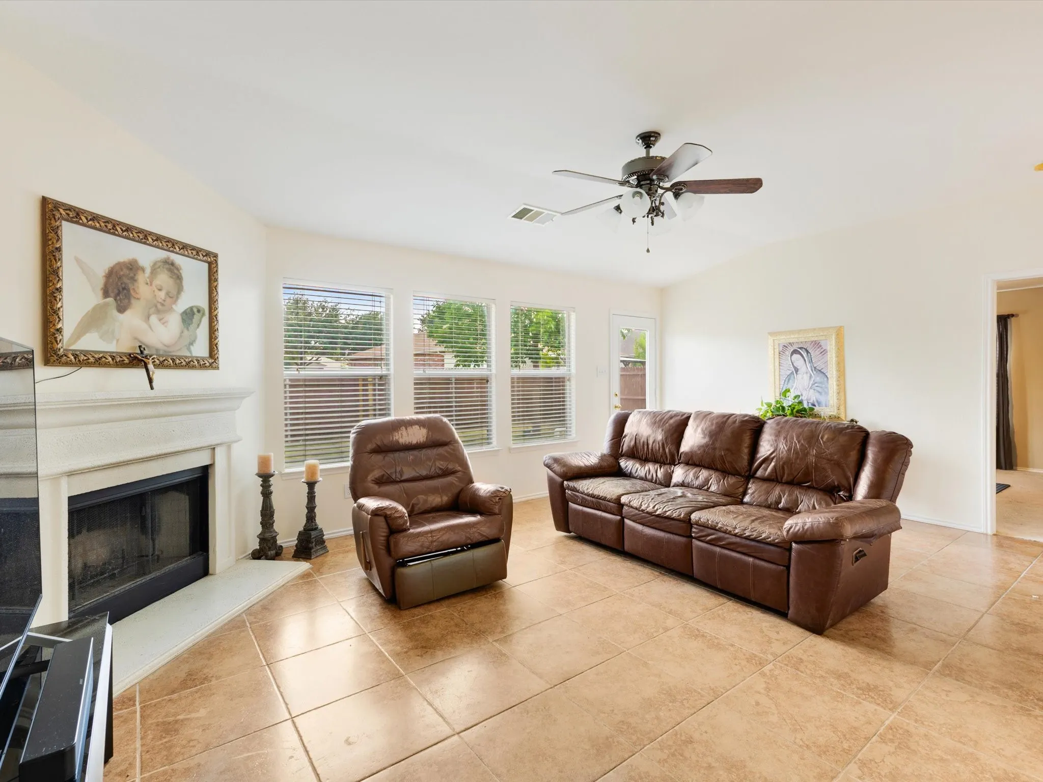 Living area featuring a fireplace with a mantel, vaulted ceiling, ceiling fan, tile flooring, and multiple windows