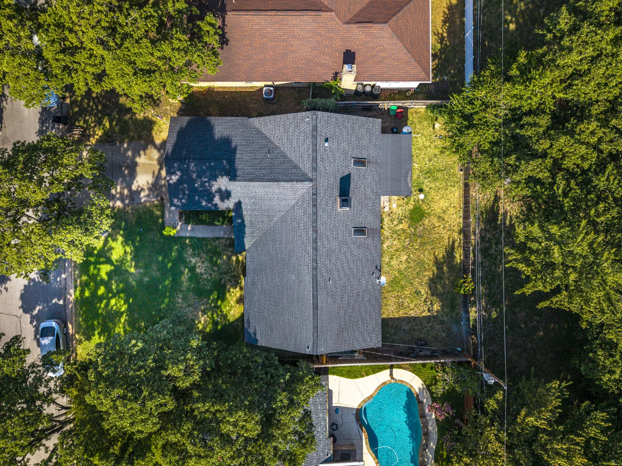 Property featuring a dark shingle roof, multiple skylights, a spacious backyard, and an inground swimming pool with a paved surround