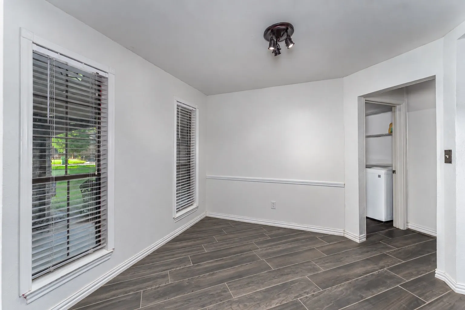 Wood-look tile flooring, two windows with blinds, white wall trim, and recessed laundry area with shelving