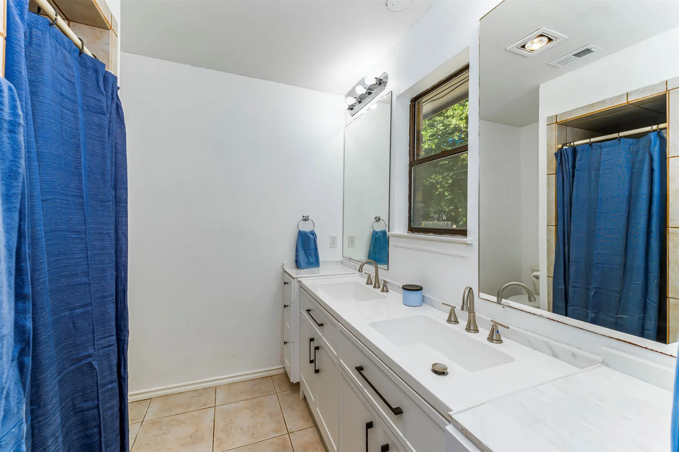 Double vanity with integrated sinks, white cabinetry with dark pulls, light-toned countertop, and tiled flooring