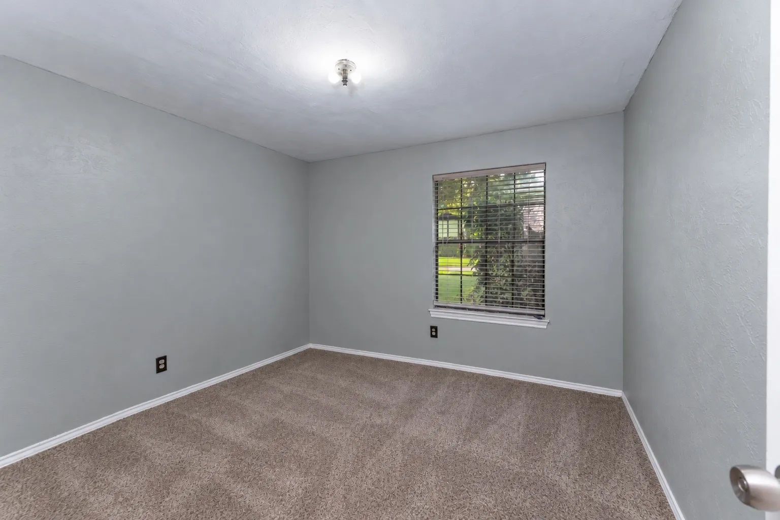 Textured walls, single window with blinds, neutral carpet, and ceiling-mounted light fixture