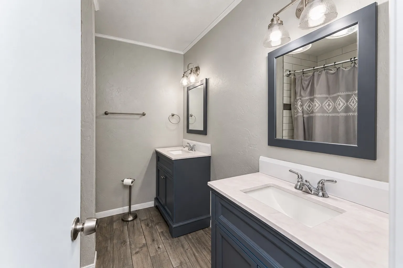 Dual vanities with integrated sinks, wood-finish flooring, white subway tile shower, and dark framed mirrors