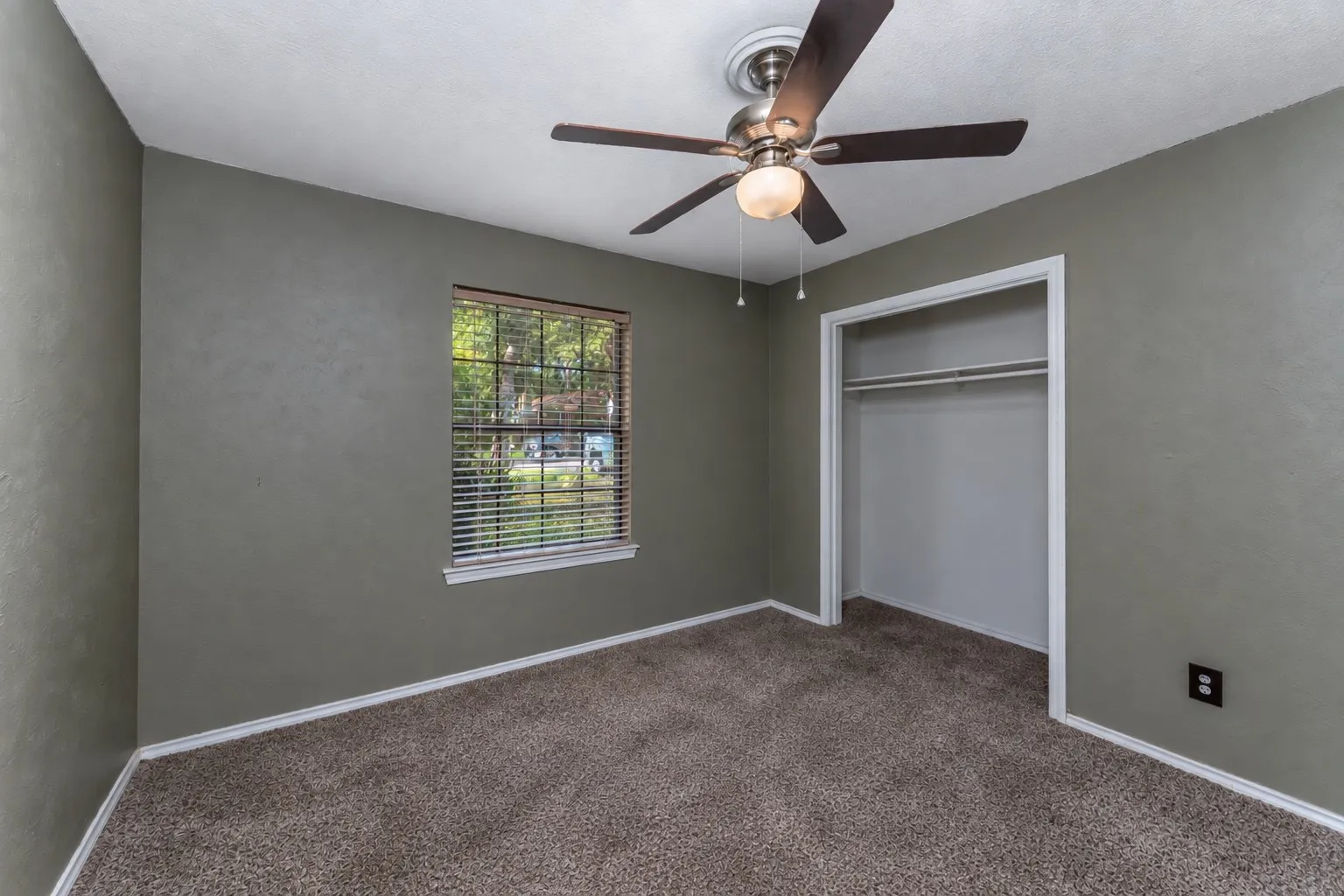 Textured walls, ceiling fan with integrated lighting, window with blinds, plush carpet, and a built-in closet with shelving