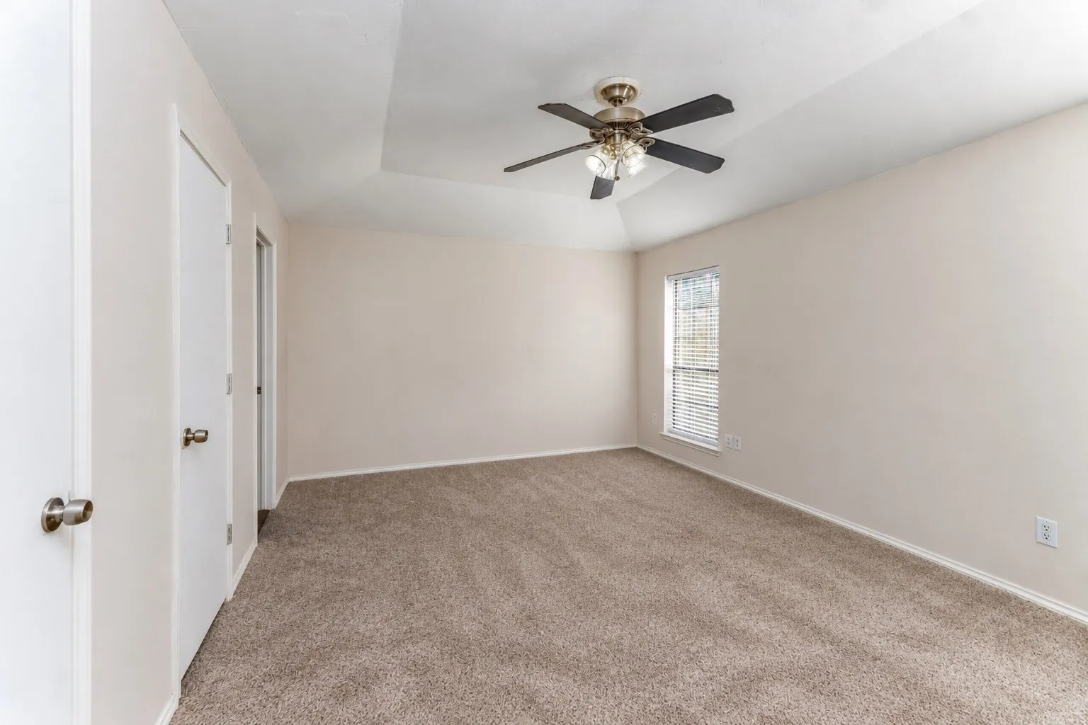 Tray ceiling with a ceiling fan light fixture, neutral carpet flooring, and a window with blinds