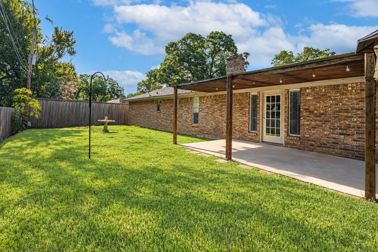 Expansive backyard featuring a brick exterior, covered patio with wood beams, concrete slab, and wood privacy fencing
