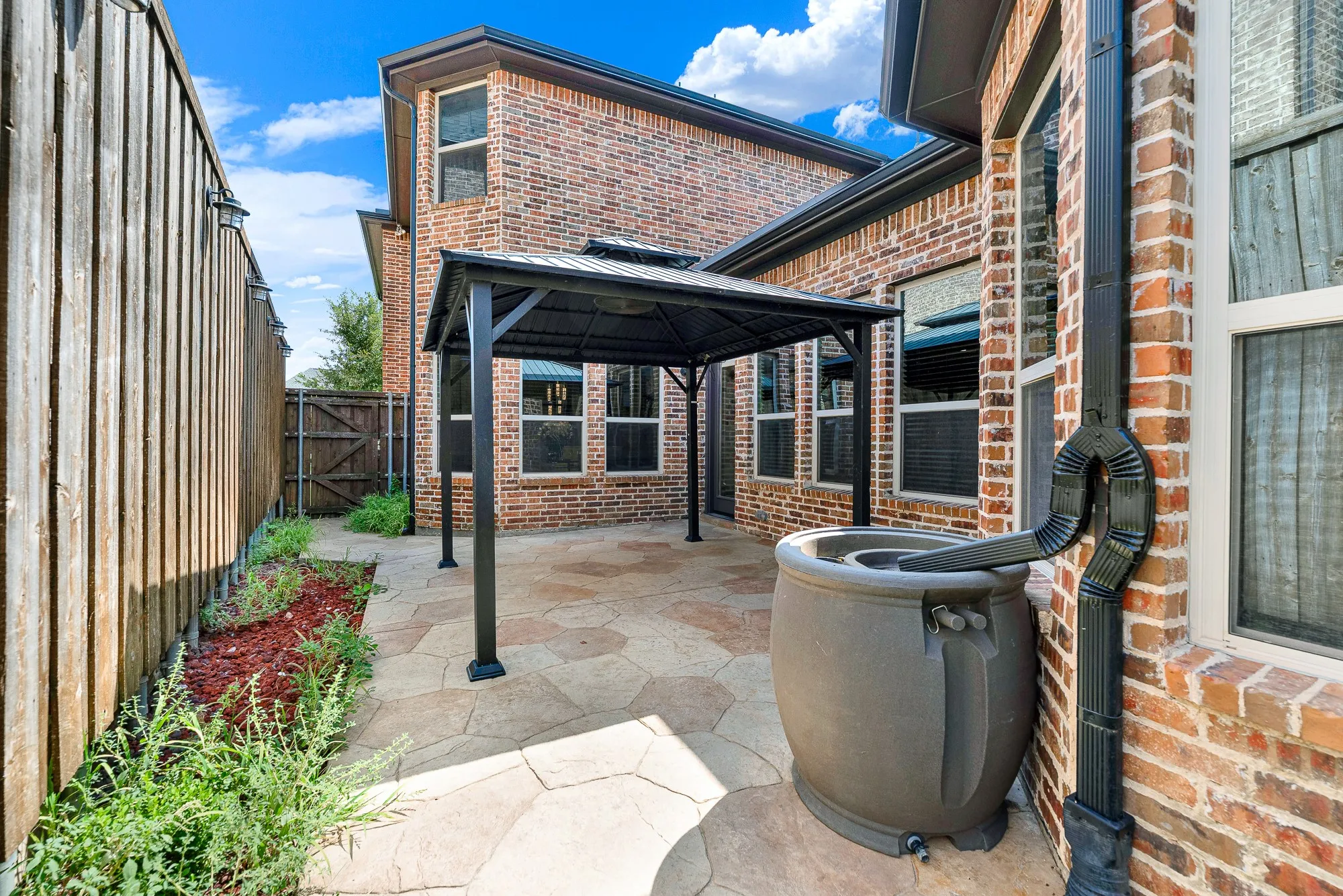 Generous rear rooflines and integrated gutter downspouts wrap around the shaded stone terrace, capturing crisp sky views above. Envision stepping outside on breezy spring afternoons to tend potted herbs and chat with neighbors across the courtyard.