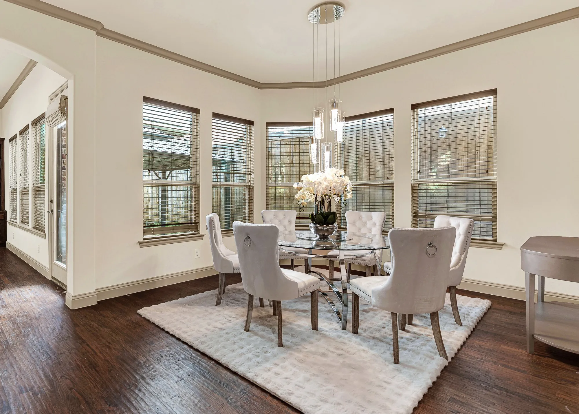 An angled bay of expansive windows wraps the nook, catching soft daylight against the rich, dark-toned flooring. Picture easy Sunday mornings here, savoring fresh coffee and warm pastries while golden rays gently filter in.