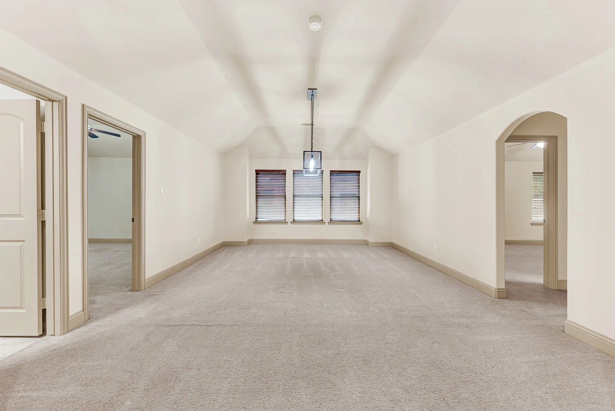 An open arched portal and symmetrical doorways flank a soaring tray ceiling, drawing daylight from the rear windows deep across the carpeted expanse. It invites energetic weekend board game tournaments or lively afternoons spent playing pool with friends.
