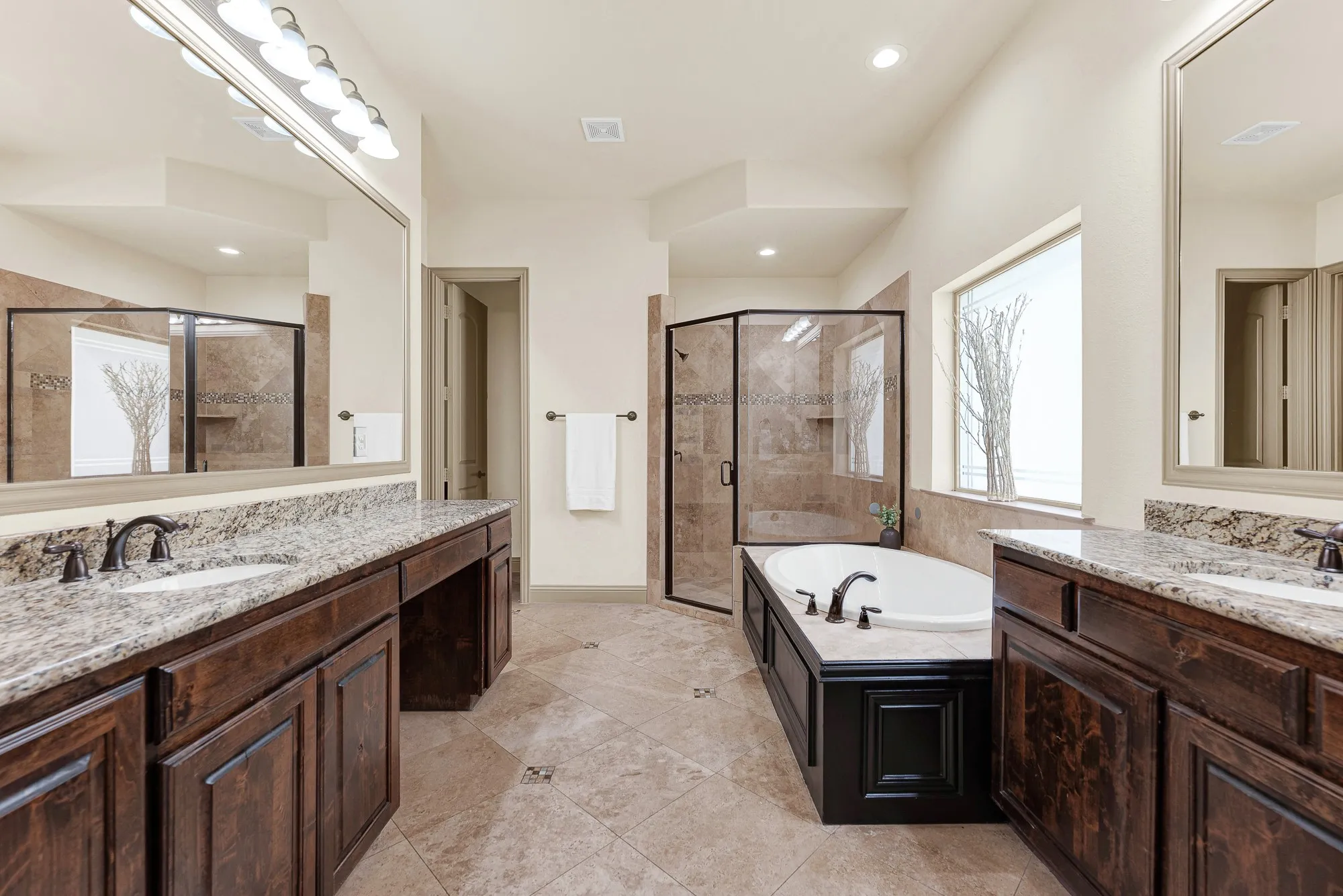 Dual granite vanities face each other across diagonal ceramic tilework, framing a raised corner glass shower stall. Picture a stress-free weekday morning routine, with plenty of private room for two people getting ready at once.