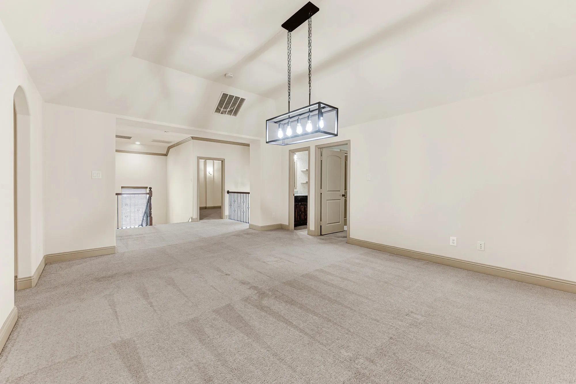 A black open-cage chandelier anchors the expansive upper landing, seamlessly framing open sights toward the wrought-iron staircase balustrade. Envision casual family gatherings drifting easily between floors during lively weekend parties.