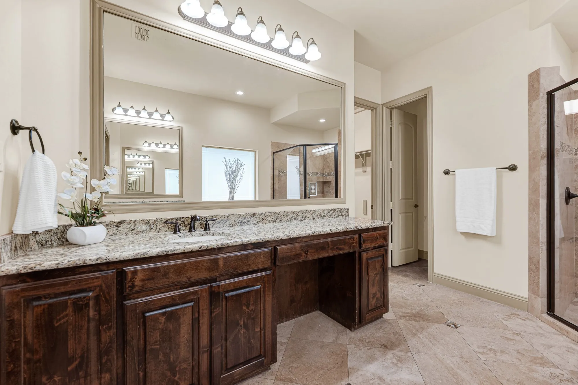 A multi-globe vanity bar illuminates the framed full-width mirror and integrated makeup knee space. It makes preparing for a night on the town feel relaxed and organized, with dedicated seating for cosmetics and grooming.