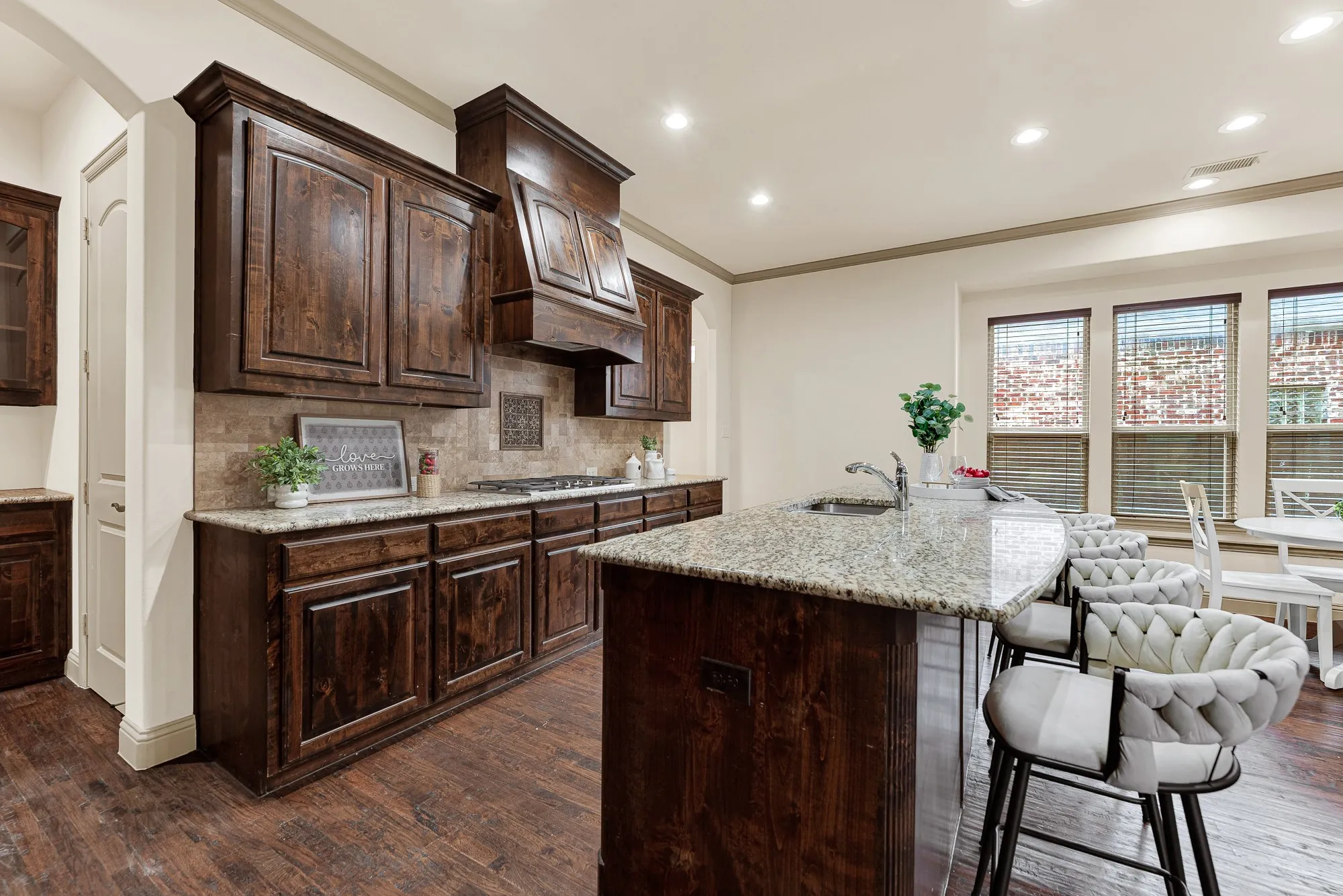 The curved breakfast counter pairs with a textured tile backsplash that catches ambient warmth from nearby side windows. Picture breezy Saturday mornings sharing freshly flipped blueberry pancakes while morning sun brightens the room.