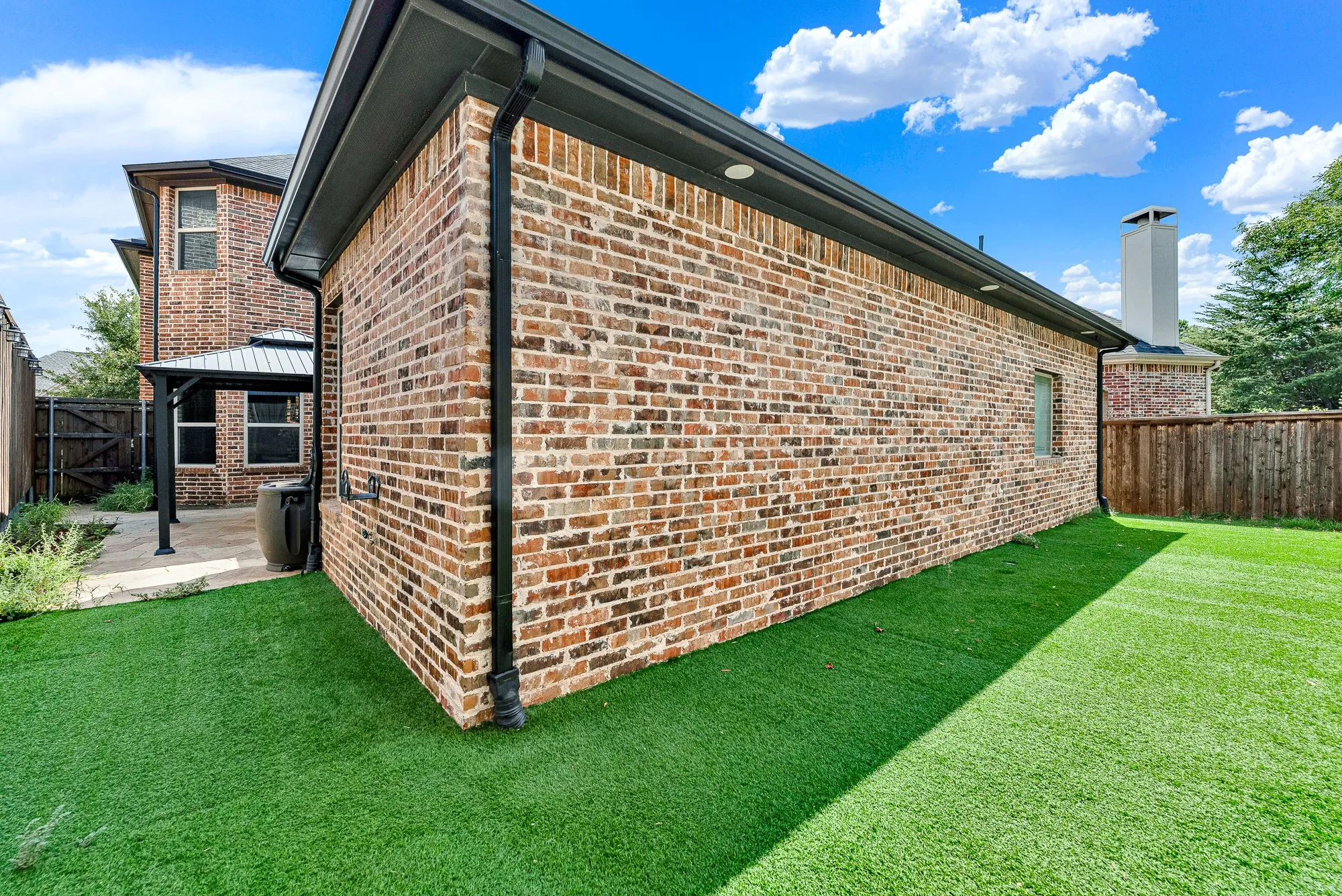Vibrant, low-maintenance synthetic turf wraps neatly around the solid brick exterior wall, framed by perimeter cedar fencing. It offers an ideal zero-upkeep green space where pets and kids can play freely without tracking mud inside.