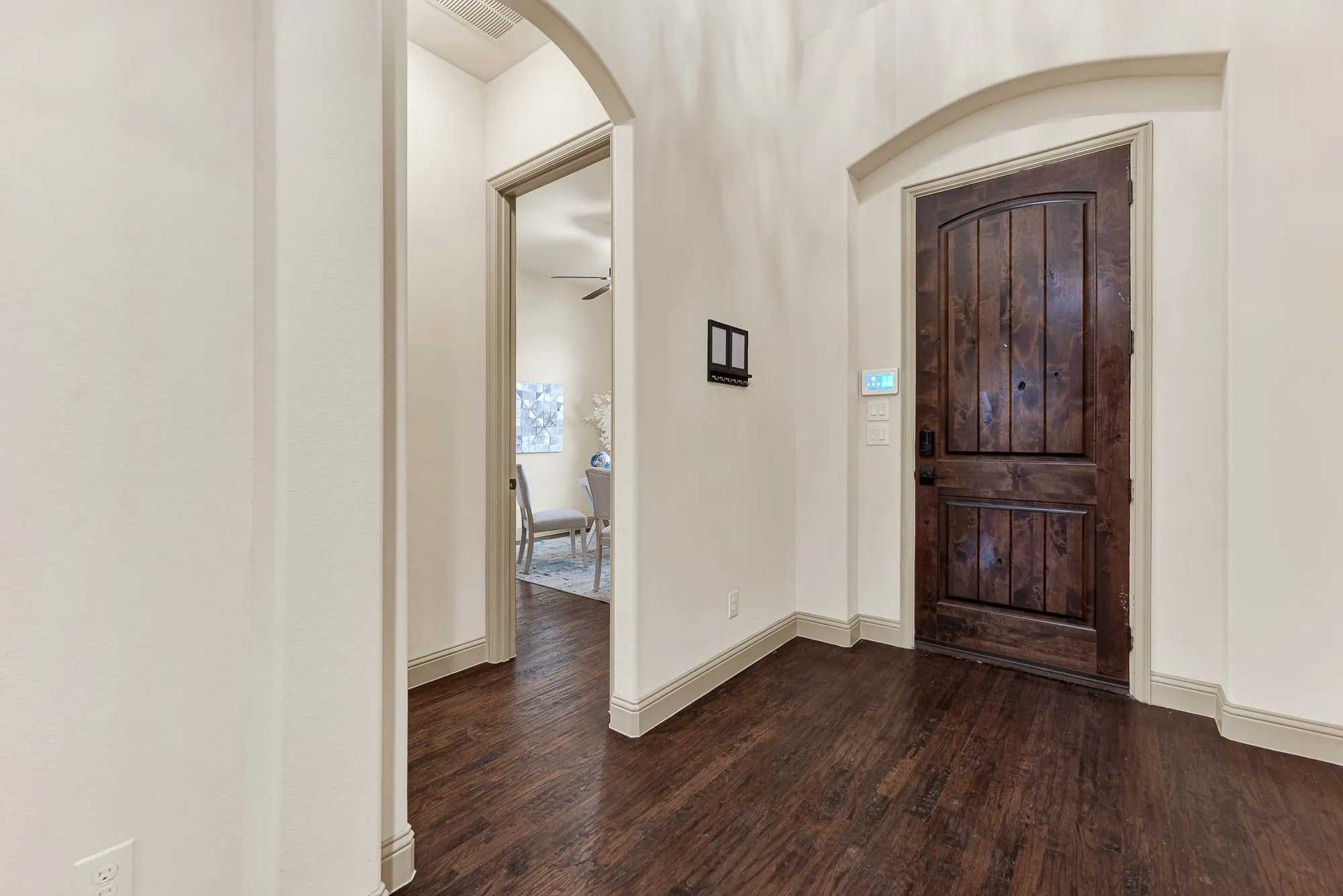 A substantial knotty-wood entry door sits recessed beneath a graceful arched niche, pairing rich grain textures with sweeping foyer lines. It marks the spot where you warmly greet arriving friends, setting an easy, hospitable mood the second they arrive.
