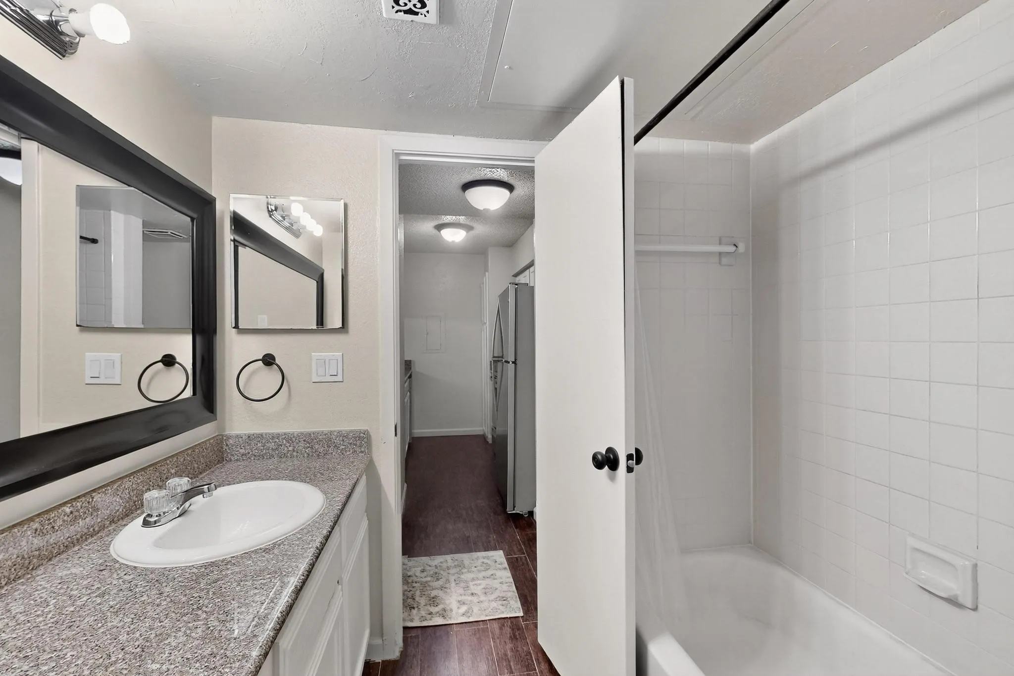 Bathroom featuring a vanity with an integrated sink, a dark framed mirror, and a tiled shower with a built-in tub