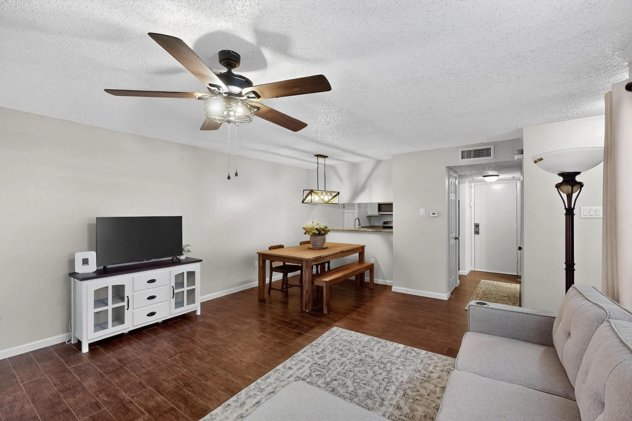 Rich wood-finish flooring, ceiling fan with integrated lighting, and a modern pendant light fixture