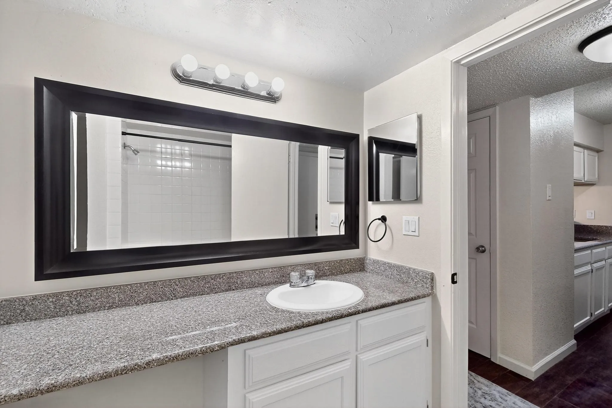 Spacious vanity with a composite countertop, an integrated sink, a large framed mirror, and a four-light fixture