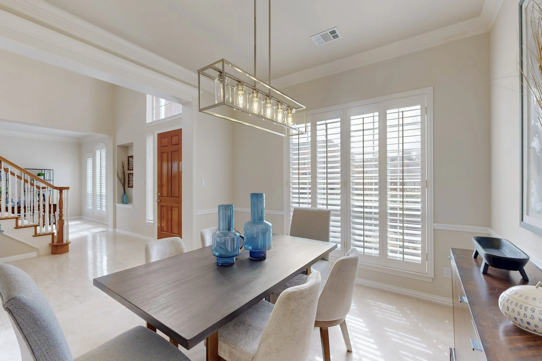Elegant formal dining room featuring soaring ceilings, plantation shutters, abundant natural light, and a contemporary designer light fixture. Photos are from previous listing when home was staged.
