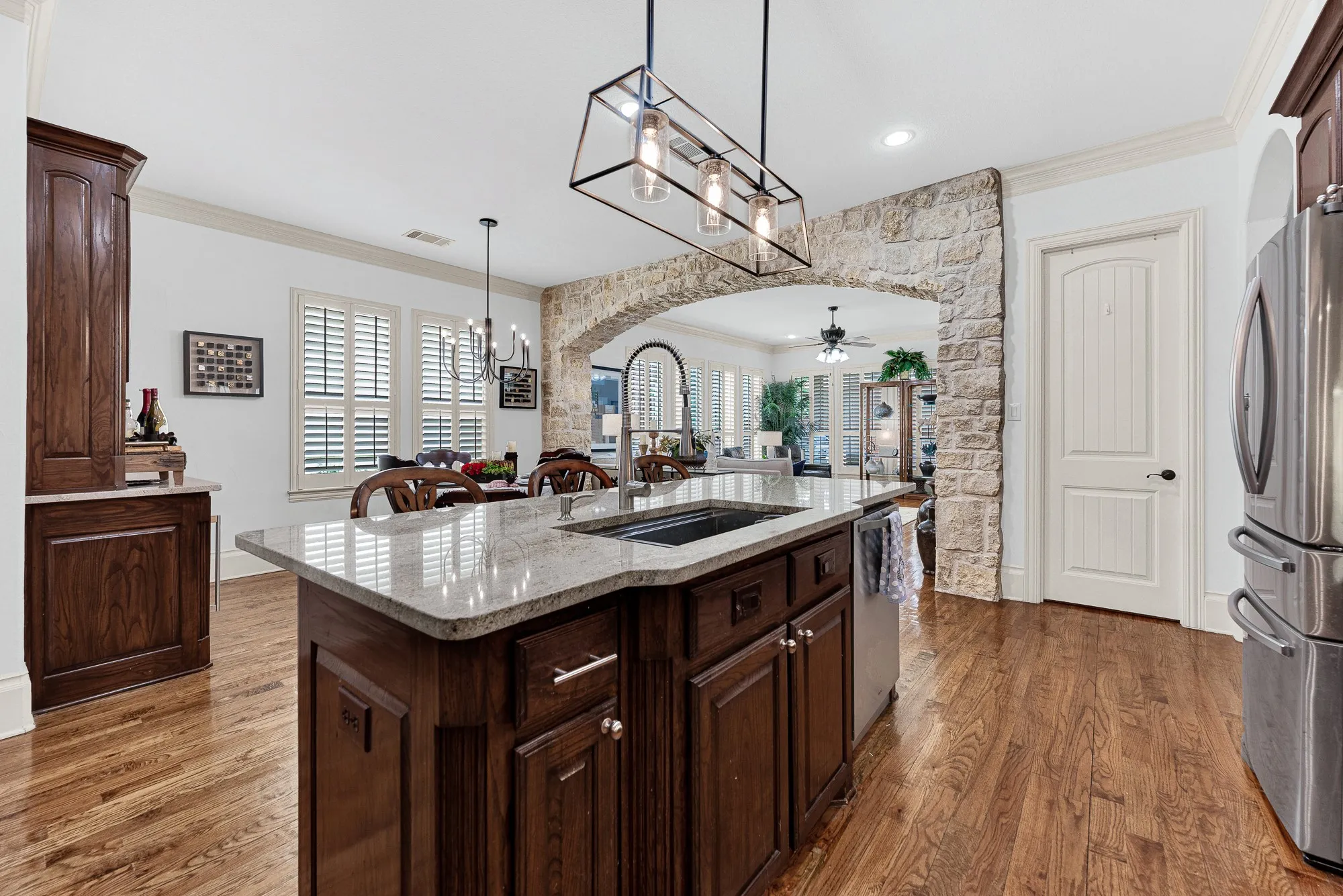 An undermount basin and pro-style faucet anchor the granite prep surface, framed by the rustic stone arch backdrop. Chat effortlessly with loved ones across the room while washing fresh produce for supper.