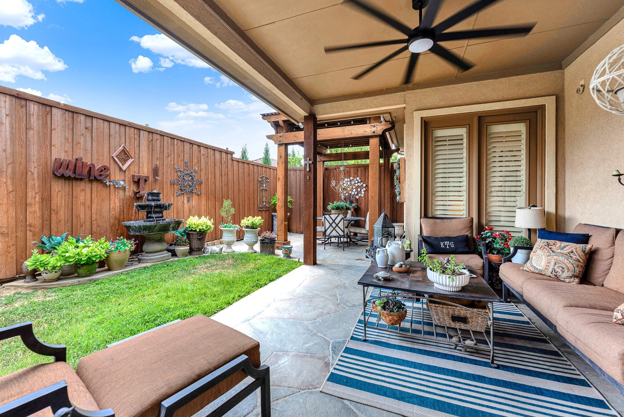 Stamped, flagstone-textured concrete extends seamlessly beneath a cooling ceiling fan and handsome wooden pergolas. Unwind after work with a chilled drink, listening to the soothing trickle of nearby water features.